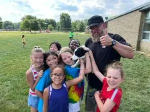 Performance Dogs of Ohio entertaining children at a birthday party, with dogs jumping through hoops and catching frisbees while kids watch and cheer