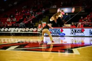 Performance Dogs of Ohio wowing the crowd at a basketball halftime show, with a frisbee dog flying high through the air to catch a disc mid-court as fans cheer in the background.